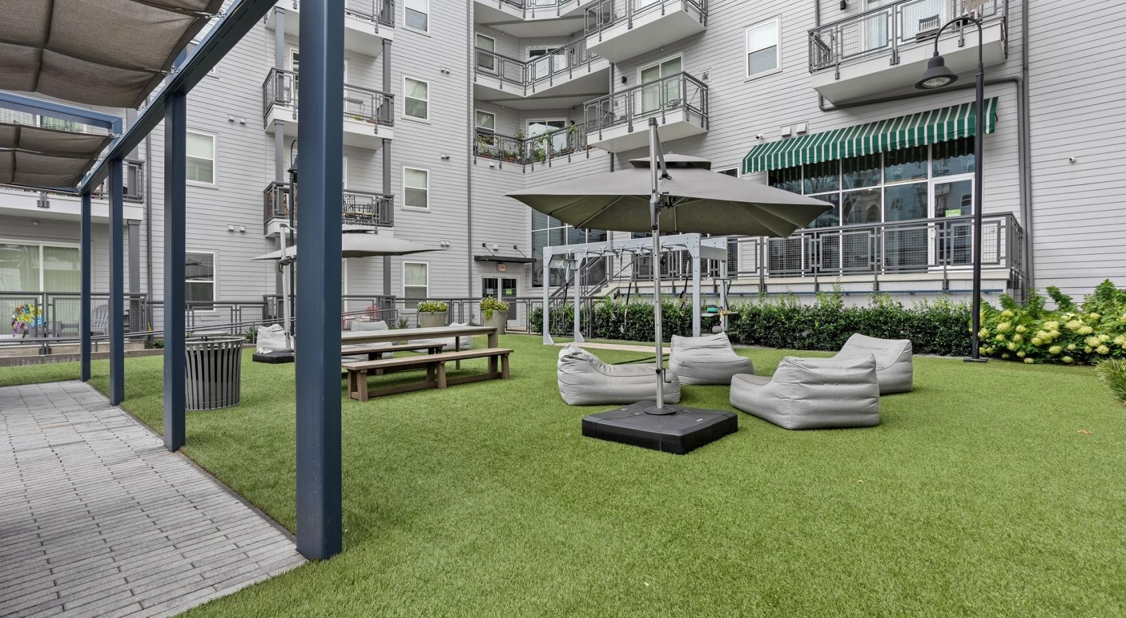 Find your perfect fit at The Cleo a large green lawn with a lounge chair and umbrella